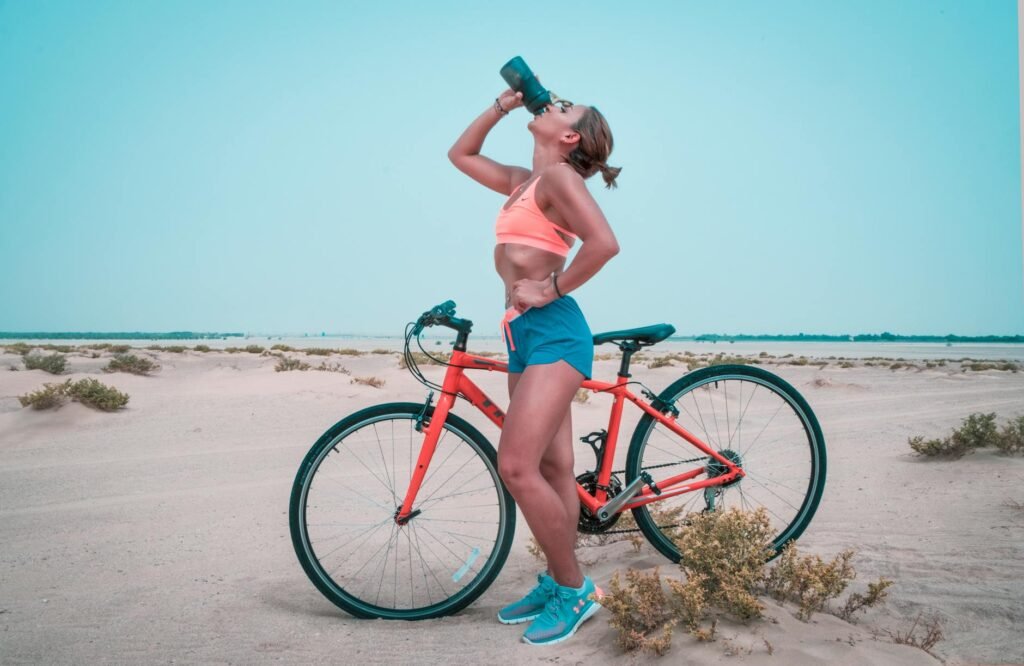 Athletic woman drinking water while biking in the Dubai desert landscape.
